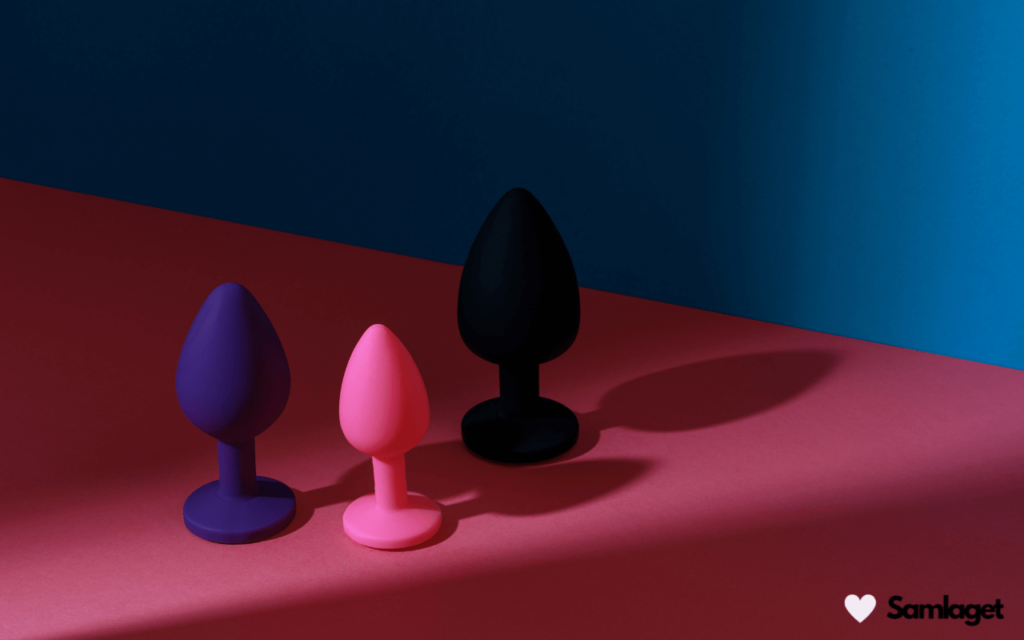 Tre analpluggar i olika storlekar och färger: lila, rosa och svart, på en färgglad bakgrund.