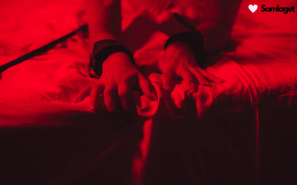 Händer i handbojor på en säng med röd belysning.