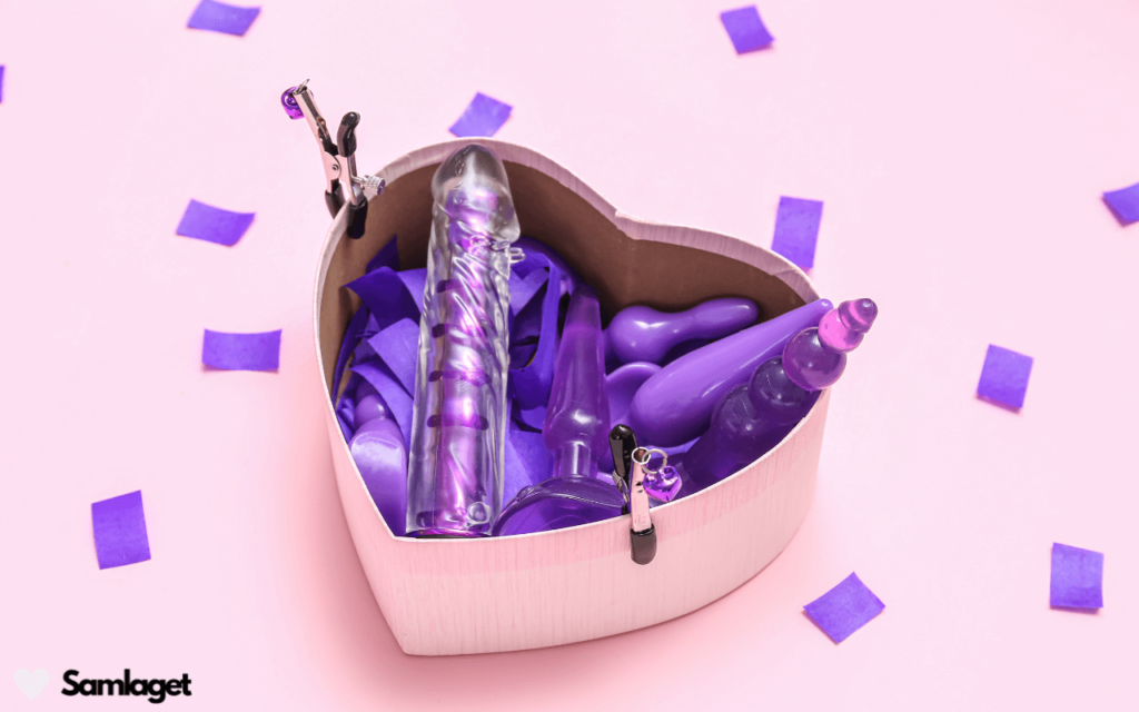 Hjärtformad låda fylld med lila och genomskinliga sexleksaker inklusive dildos och analpluggar.